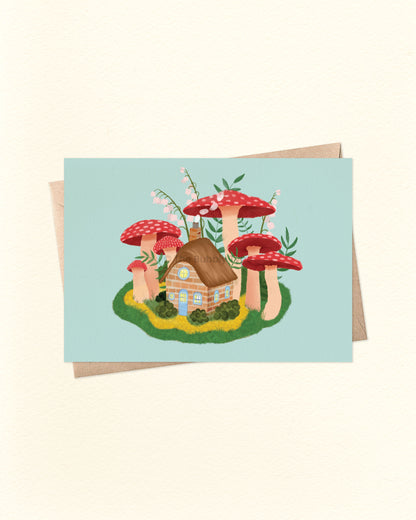 Front of A6 landscape greeting card featuring a whimsical illustration of a cosy cottage surrounded by colourful mushrooms. Perfect for fantasy lovers, nature fans, or as a unique housewarming card. Shown with a brown kraft envelope. A magical, Australian made card by The Bubbly Type.