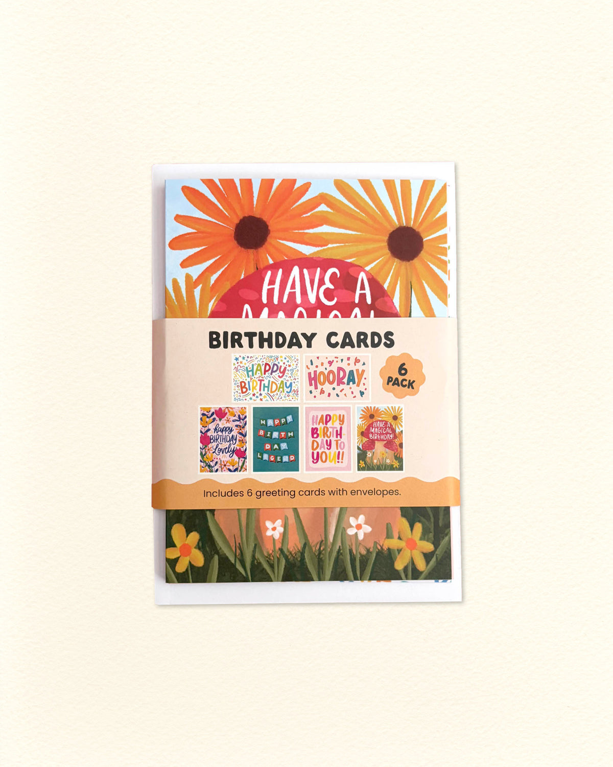A 6-pack of 'Have a Magical Birthday Cards' in floral envelopes, featuring a white package with orange daisy illustrations and previews of colourful cards inside, set against a warm cream background.
