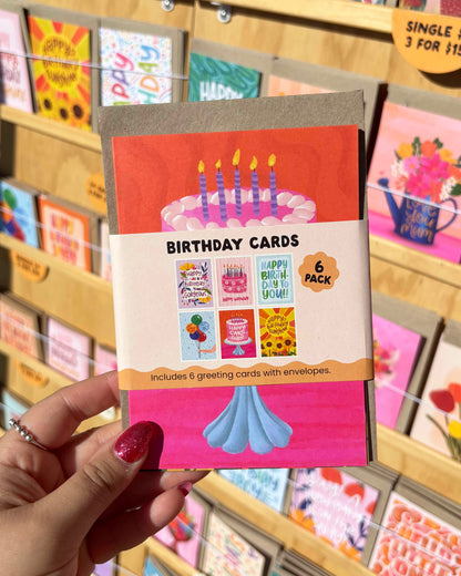 Pack of birthday cards held by a hand with a blurred store display in the background