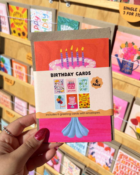 Pack of birthday cards held by a hand with a blurred store display in the background