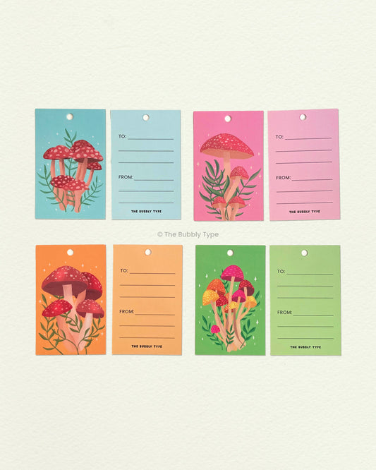 All four mushroom gift tags laid flat showing front and back. Features botanical and forest-inspired illustrations. Ideal for earthy, thoughtful gifting.