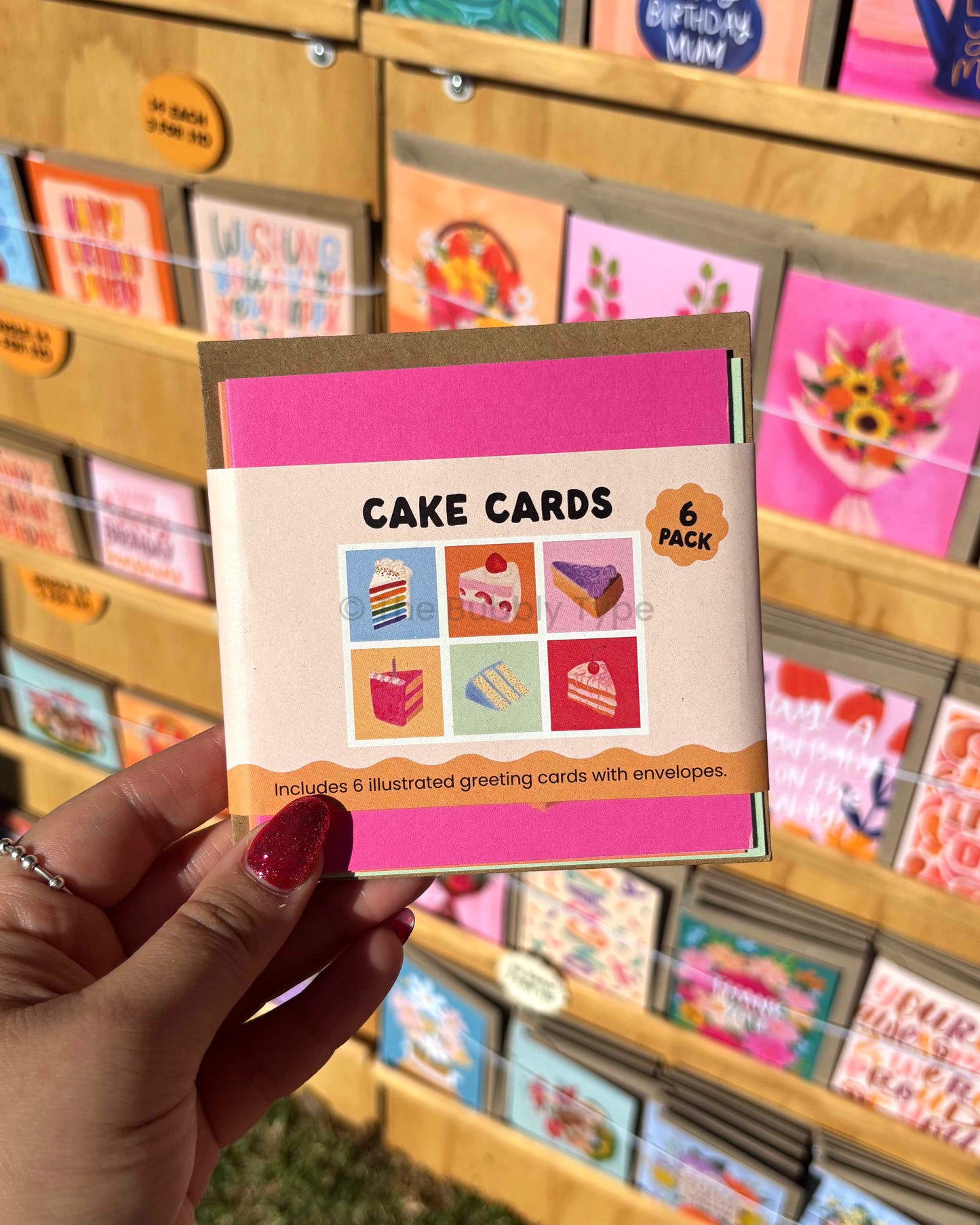 Hand holding a pack of cake-themed greeting cards with a store display in the background.