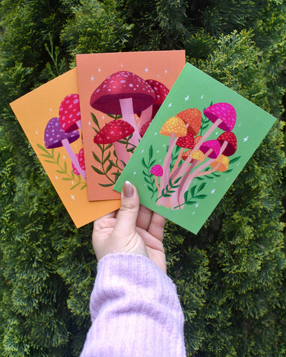 Three colourful mushroom-themed cards held by a hand against a green leafy background