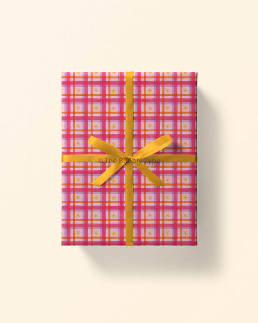Top view of a gift wrapped in pink daisy gingham wrapping paper, showing yellow daisies on a pink checkered pattern. Perfect gift wrap for girls and friends to celebrate birthdays or any fun occasion.