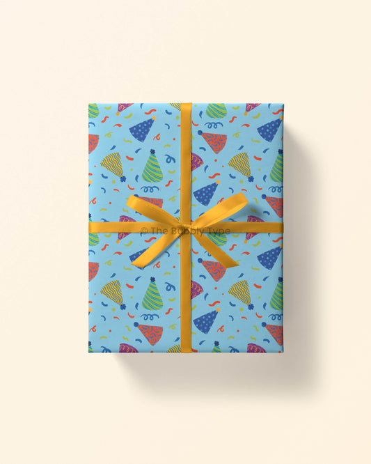 Top view of a gift wrapped in party hat wrapping paper, decorated with colourful birthday hats and confetti. This gift wrap is perfect for celebrating boys birthdays. Wrapping is printed on 100% recycled paper in Australia. Boys birthday wrapping paper.