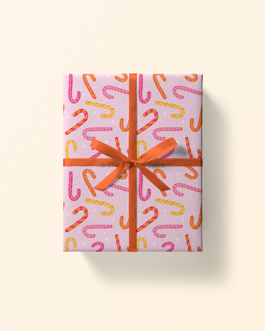 Top view of a gift wrapped in pink candy cane wrapping paper featuring red and white candy canes on a soft pink background.
