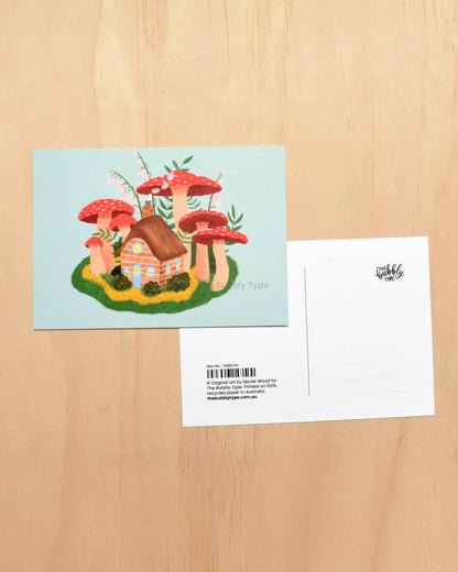 Postcard with a mushroom house illustration on a wooden surface
