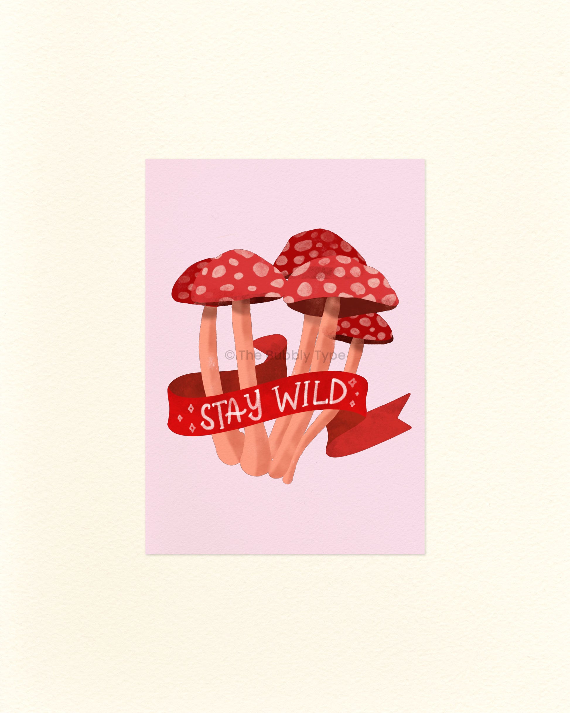 A postcard featuring an illustration of red mushrooms with white spots and a 'Stay Wild' banner on a light pink background