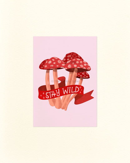 A postcard featuring an illustration of red mushrooms with white spots and a 'Stay Wild' banner on a light pink background