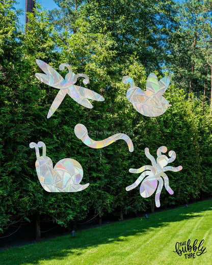 Iridescent dragonfly, butterfly, snail, and spider sun catcher window stickers against a green forest background.