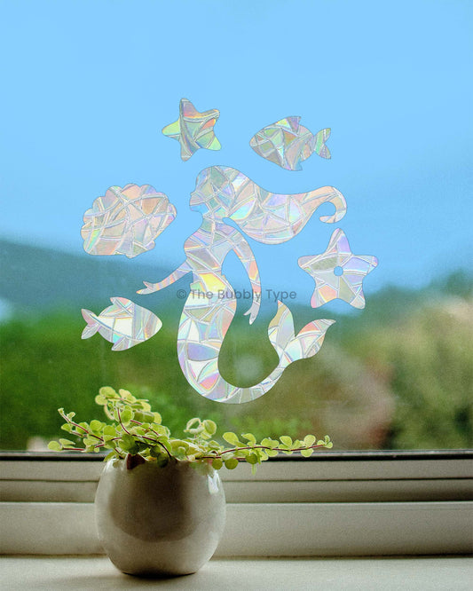 Decorative sun catcher window stickers of a mermaid and fish on a window with a blurred outdoor background.