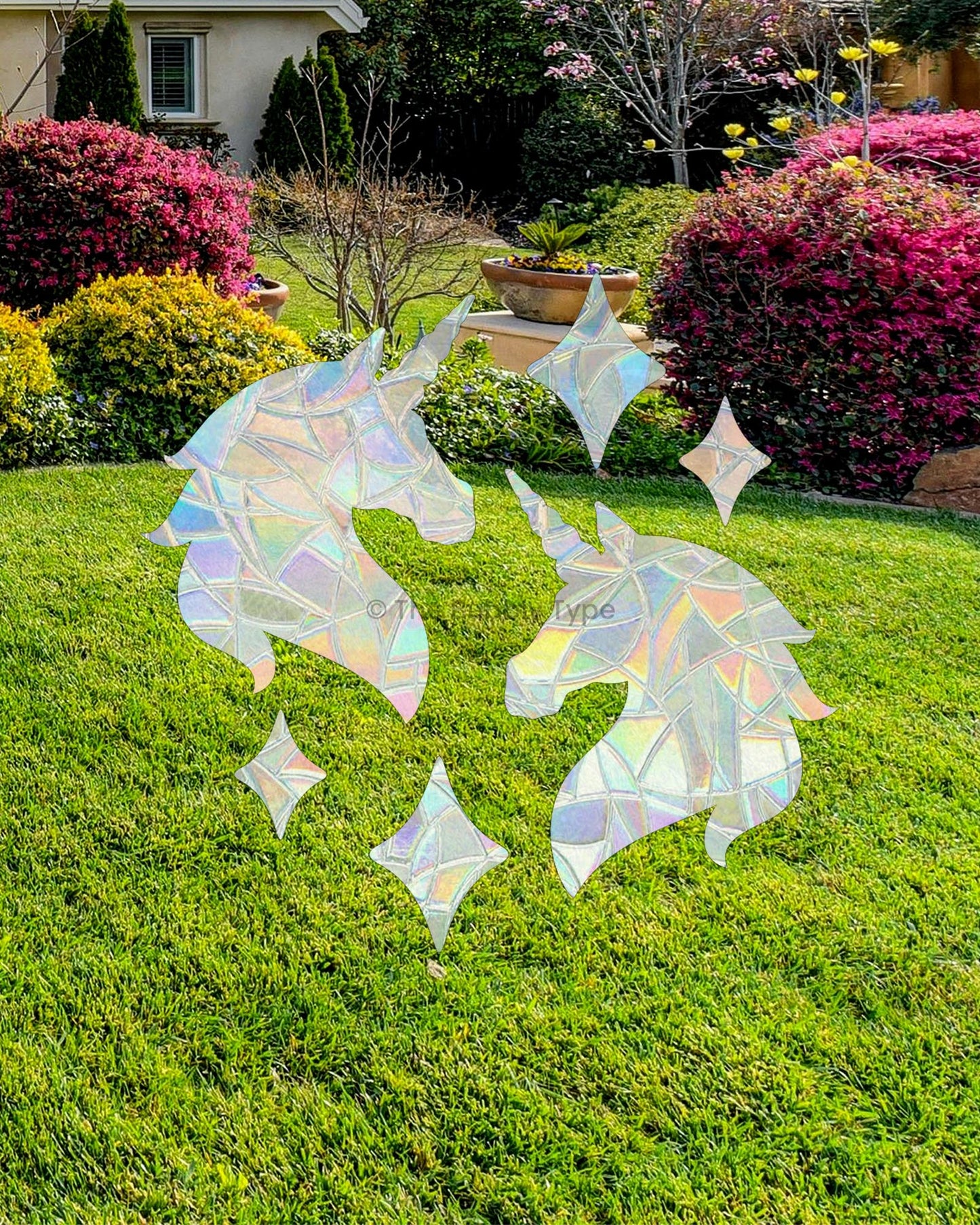 Iridescent unicorn and star-shaped sun catcher stickers on a window with grassy garden background.