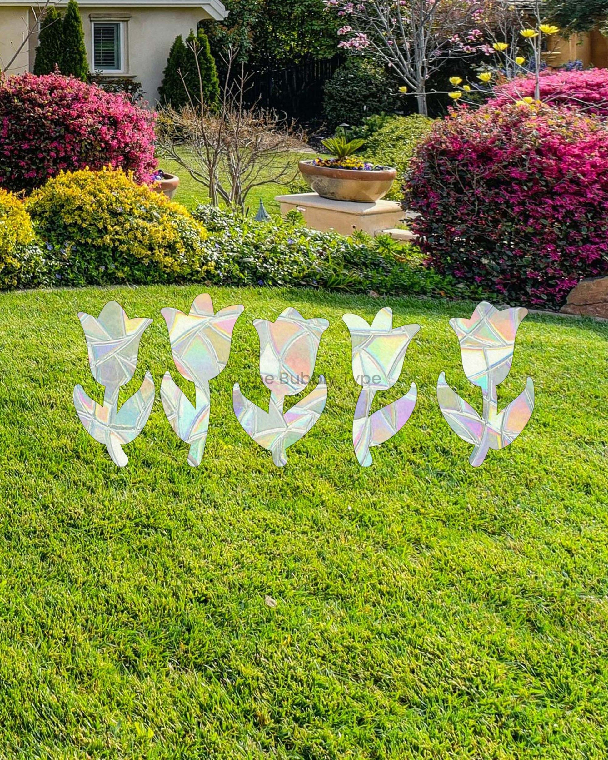 Decorative sun catcher window stickers shaped like tulips flowers on a grassy lawn with a garden and house in the background.