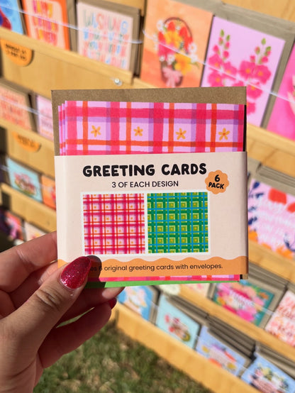 Pack of greeting cards with a hand holding it, set against a background of more greeting cards.