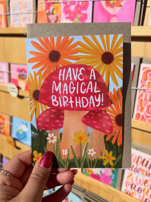 Card with mushrooms and flowers and 'Have a Magical Birthday!' text held by a hand.