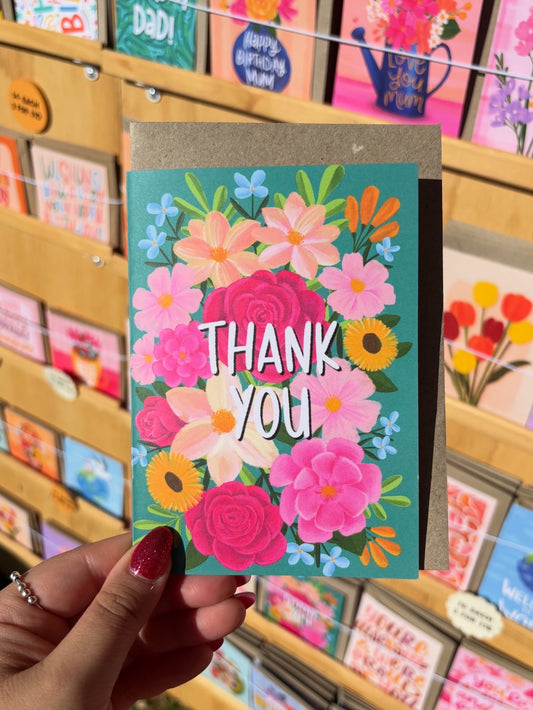 Colourful 'Thank You' card held by a hand with a background of various greeting cards.