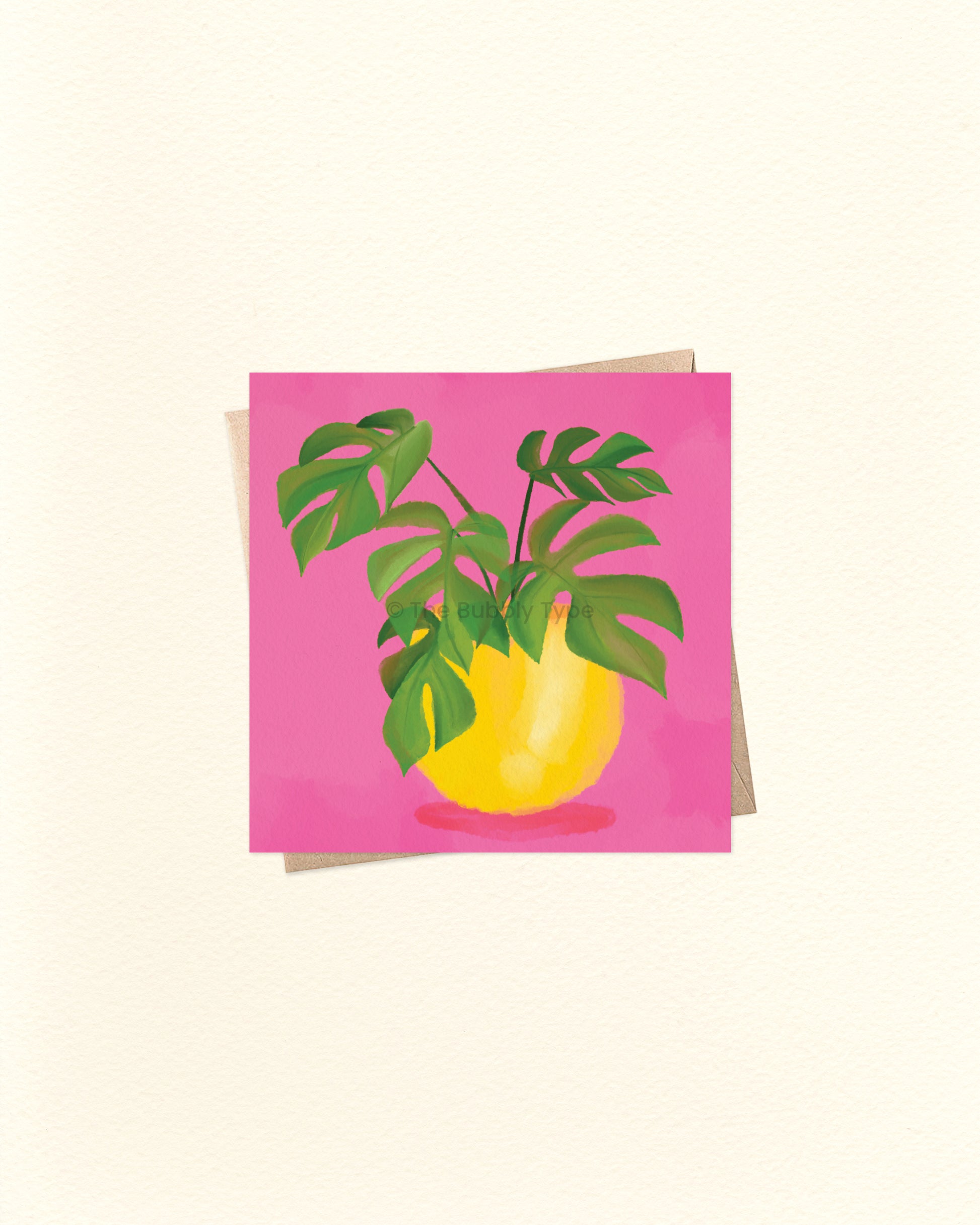 A square card featuring a stylised illustration of a yellow vase with green monstera leaves against a bright pink background, shown on a light cream textured surface with an envelope partially visible behind it.