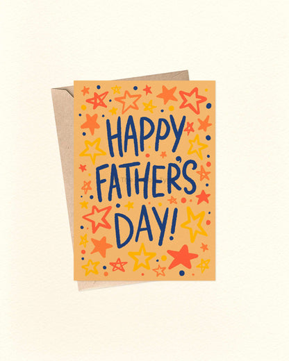 An A6 Father's Day greeting card with a kraft envelope behind it, featuring the words 'HAPPY FATHER'S DAY!' in dark blue lettering surrounded by colourful hand-drawn stars and dots on a warm orange background.