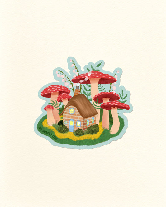A whimsical illustrated vinyl sticker featuring a small brick house surrounded by oversized red-and-white mushrooms, green foliage, and a light blue outline, centred on a warm off-white background.