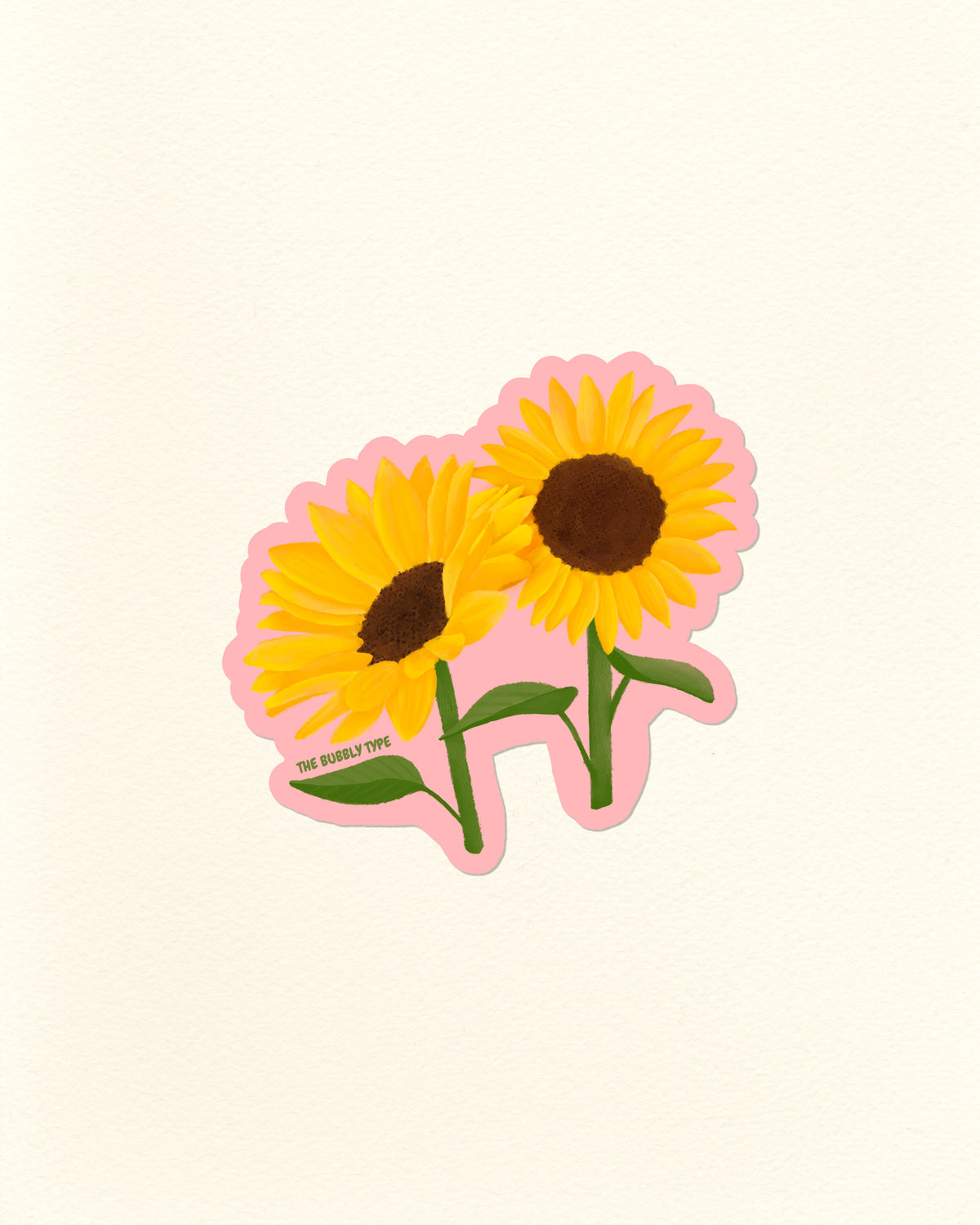 A die-cut sticker featuring two yellow sunflowers with brown centers, green stems, and a pink outline, shown on a plain off-white background. Small text near the lower left reads 'THE BUBBLY TYPE'.
