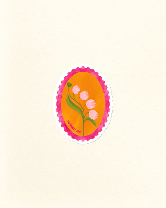 A die-cut sticker featuring a stylised lily of the valley flower illustration, set against a bright orange oval background with a pink scalloped postage stamp border, shown on a textured off-white paper background.