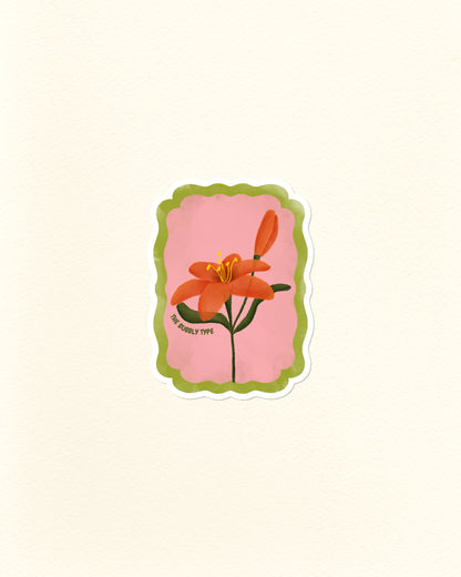 A die-cut postage stamp sticker featuring an orange lily flower on a pink background with a scalloped green border, shown on a textured off-white paper background.