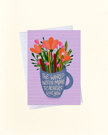 A greeting card with a lavender striped background featuring an illustration of orange flowers, pink blossoms, and colorful pencils emerging from a blue mug. The mug has the text 'THE WORLD NEEDS MORE TEACHERS LIKE YOU' written on it.