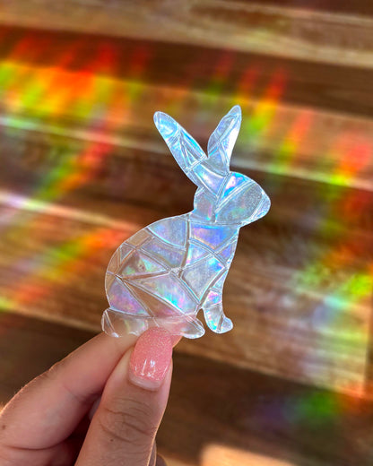 Iridescent rabbit-shaped sun catcher window sticker held by a hand with a colourful, rainbow lights, blurred background