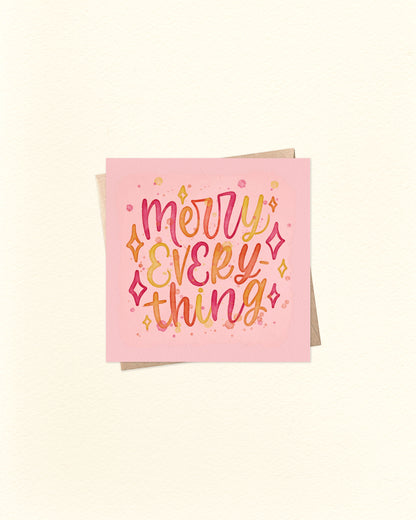 Christmas greeting card in square shape with 'Merry Everything' text on a pink background and a brown kraft envelope