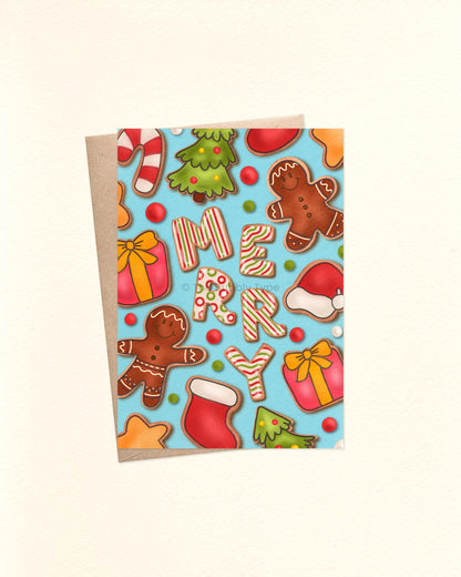 A6 Christmas card with a blue background and hand-illustrated design of festive gingerbread cookies decorated in colourful icing. In the centre, five cookies shaped like letters spell out “MERRY.” Surrounding cookies include candy canes, presents, stars, Christmas trees, Santa hats, and gingerbread people. A brown kraft envelope peeks out from underneath the card.