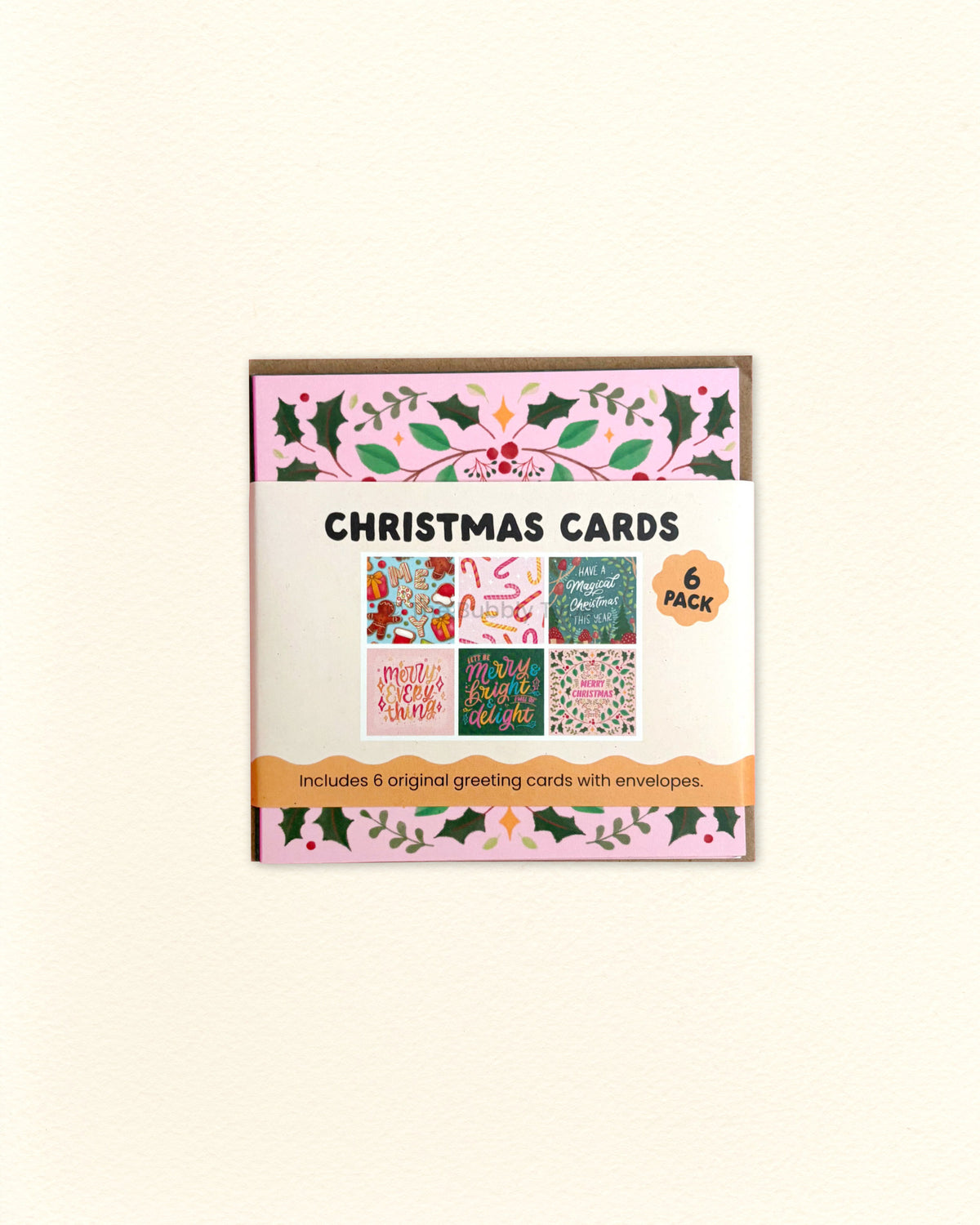 A boxed set of Christmas greeting cards shown against a plain light beige background. The package has a pink and green holly border and reads 'CHRISTMAS CARDS' with '6 pieces' and 'Includes 6 original greeting cards with envelopes' on the front.