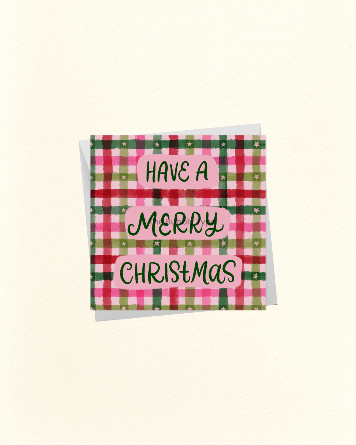 A square Christmas greeting card with a pink, green, and red plaid pattern and the words 'HAVE A MERRY CHRISTMAS' in black script on pink labels, shown on a cream background.