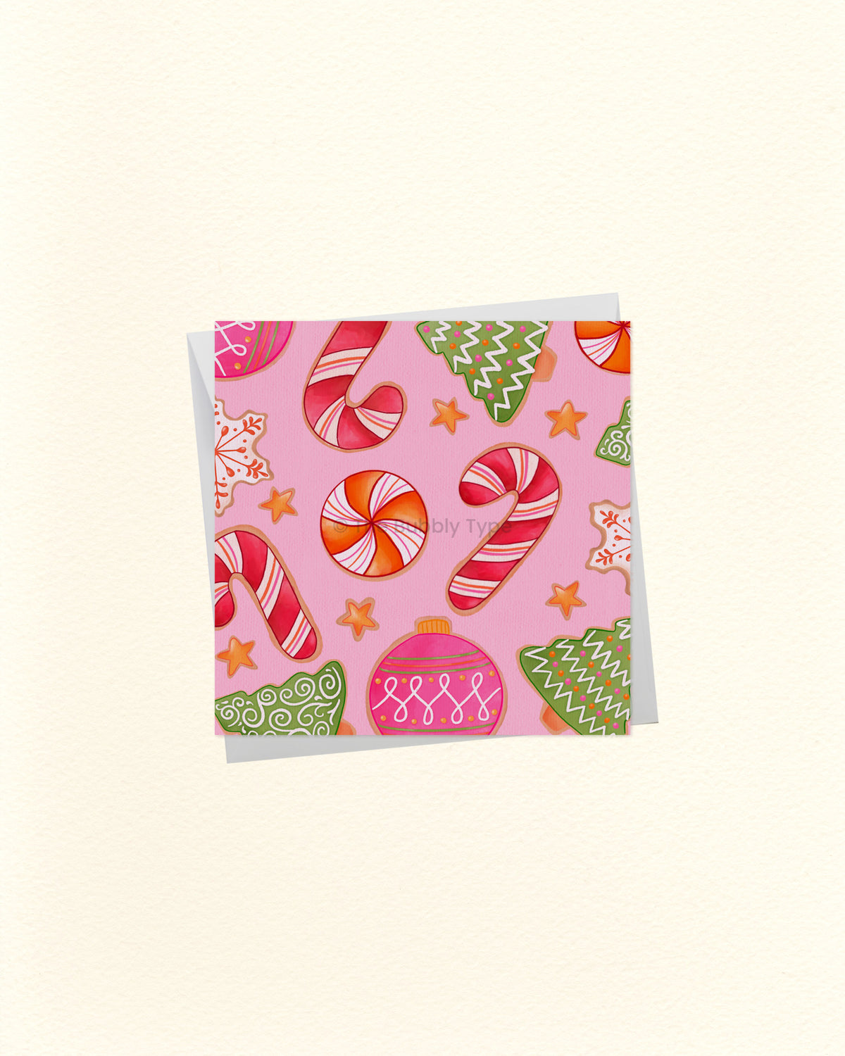 A square greeting card with a pink background and a festive holiday pattern featuring candy canes, ornaments, stars, and gingerbread cookies, shown on a light cream background.