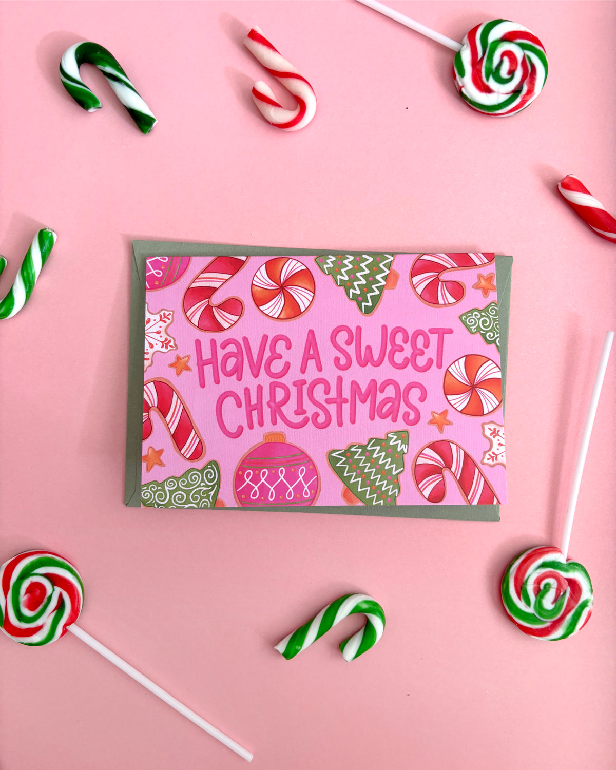 A Christmas greeting card with the text 'Have A Sweet Christmas' in pink lettering, surrounded by candy canes, lollipops, and peppermint candies on a pink background.