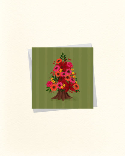 A square greeting card with a green striped background and a colourful floral tree illustration in the centre, shown with a white envelope behind it on a light cream background.