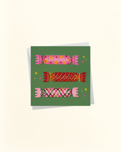 A square art print or card featuring three stylized pink and red candy illustrations on a muted green background, shown against a warm off-white backdrop with a soft shadow.