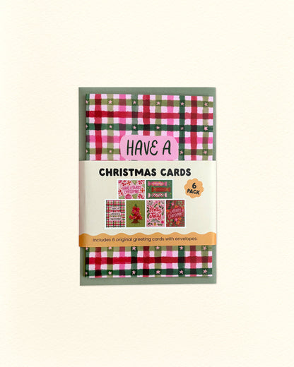 A package of 6 Christmas cards featuring festive red, green, and pink plaid patterns, shown on a light cream background.
