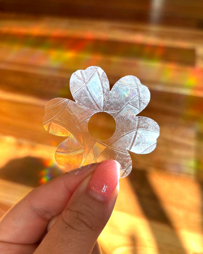 Hand holding a transparent flower-shaped sun catcher rainbow maker with a colourful background