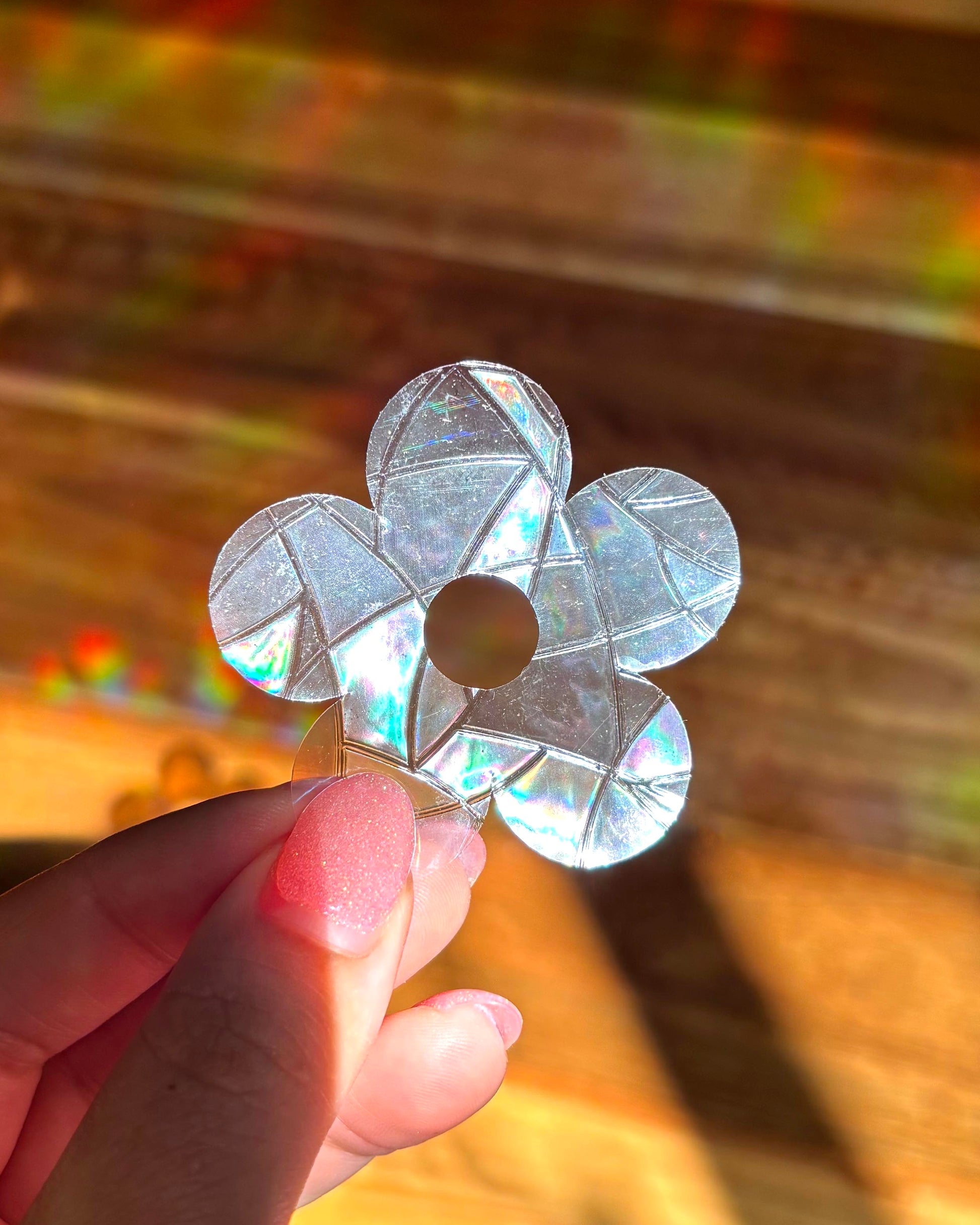 Iridescent flower-shaped sun catcher held by a hand with a blurred background