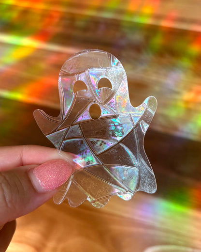 Holographic ghost-shaped sun catcher window sticker held by a hand with a multicolored background