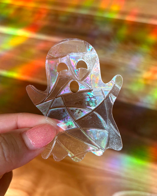 Holographic ghost-shaped sun catcher window sticker held by a hand with a multicolored background