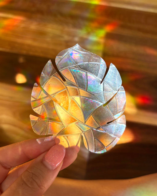Hand holding a decorative glass cling sun catcher with iridescent colours against a blurred background