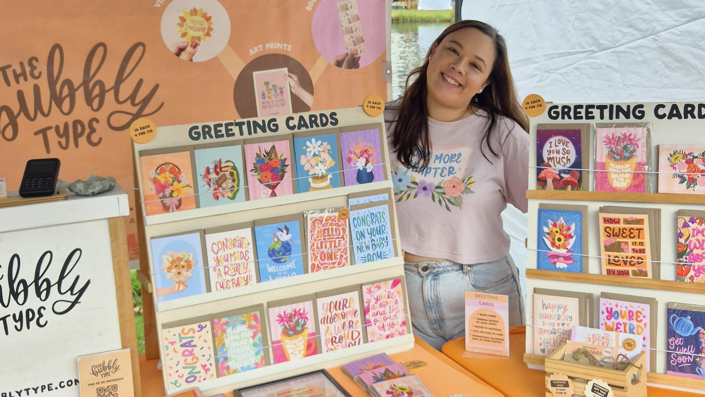 Nicole standing behind her craft market display of colourful greeting cards.