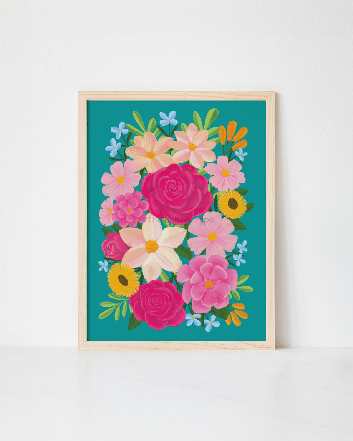 A framed floral art print featuring a colourful bouquet of pink, yellow, and white flowers on a teal background, set in a light wood frame against a white wall.