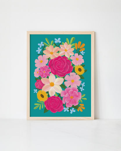 A framed floral art print featuring a colourful bouquet of pink, yellow, and white flowers on a teal background, set in a light wood frame against a white wall.
