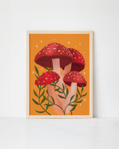 A framed art print featuring a whimsical illustration of four red mushrooms with white spots and green leaves on a warm orange background, displayed against a clean white wall.