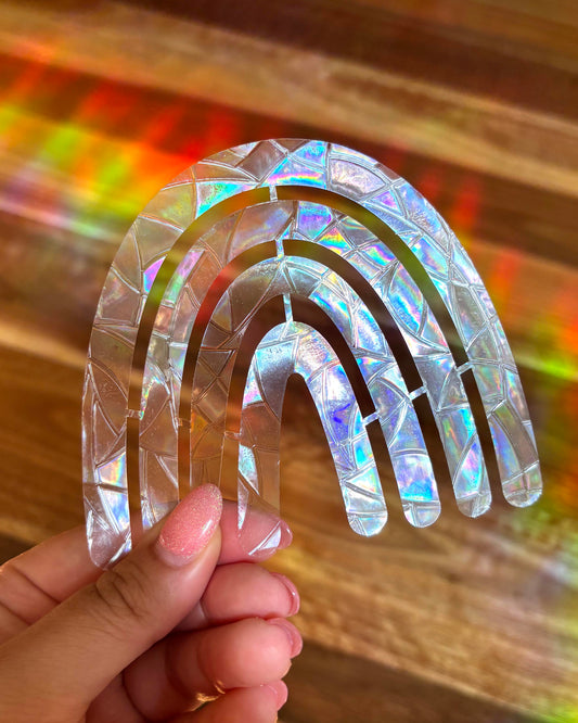 Holographic rainbow-shaped sun catcher window sticker held by a hand with a colourful background