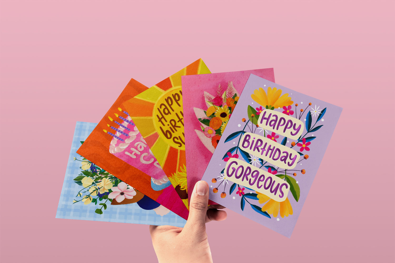 A hand holding a selection of vibrantly colour greeting cards, ranging from birthday cards to floral designs and more. All card have been designed and printed in Australia on 100% Recycled Papers. Wholesale Australian Made Stationery & Gifts bulk buy.