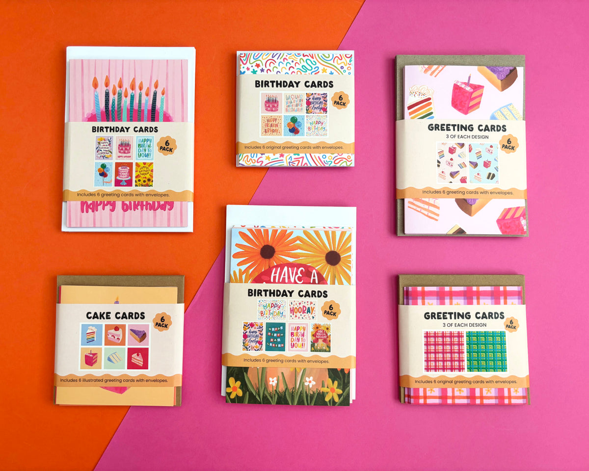 Six greeting and cake card packs arranged in two rows on a diagonally split orange and pink background. The cards feature colourful birthday-themed illustrations, including candles, cupcakes, sunflowers, and plaid patterns, with text such as 'BIRTHDAY CARDS,' 'GREETING CARDS,' and 'CAKE CARDS.
